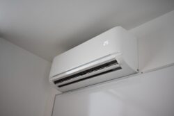 A white wall-mounted air conditioner displays a temperature of 25 degrees Celsius in a minimalist room.