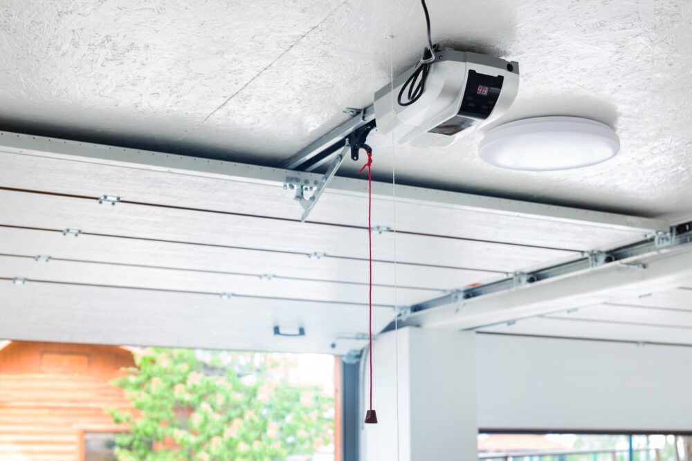 Garage door opener mounted to a ceiling above a white sectional garage door.