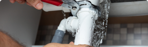 Plumber tightening leaky pipe with wrench